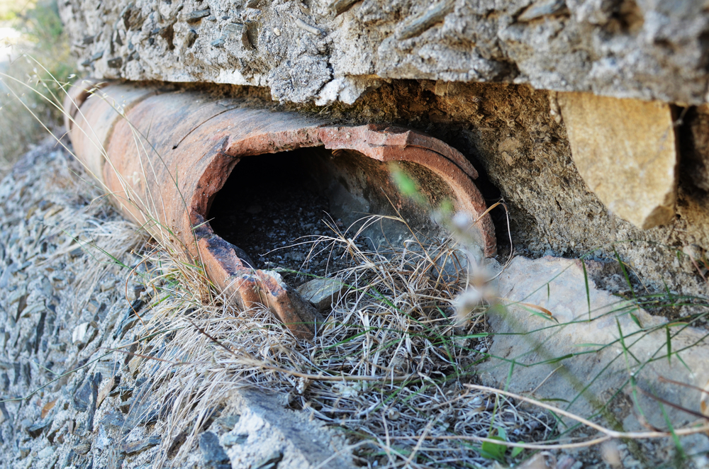 a cracked underground clay sewer line showing rainwater from saturated soil leaking through a crack, causing water levels to rise and flow backward toward a residential home.