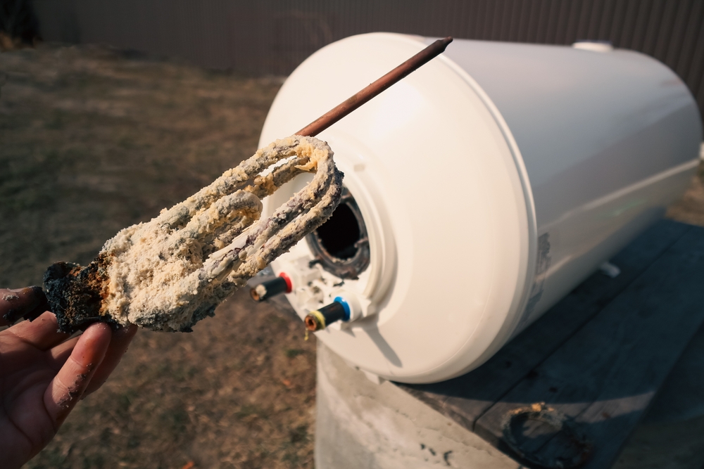 a water heater tank showing sediment buildup trapping steam bubbles causing the Kettle Effect noise, next to a technician preparing a tank flush.